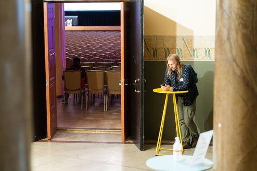 One man with long hair leans against a table in the foyer